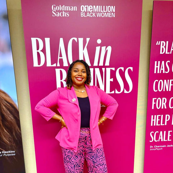 Woman in pink outfit posing in front of a 'Black in Business' banner with Goldman Sachs and ONE MILLION BLACK WOMEN logos.